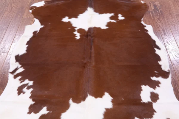 Real brown and white cowhide rug laid on hardwood floor in full-room view